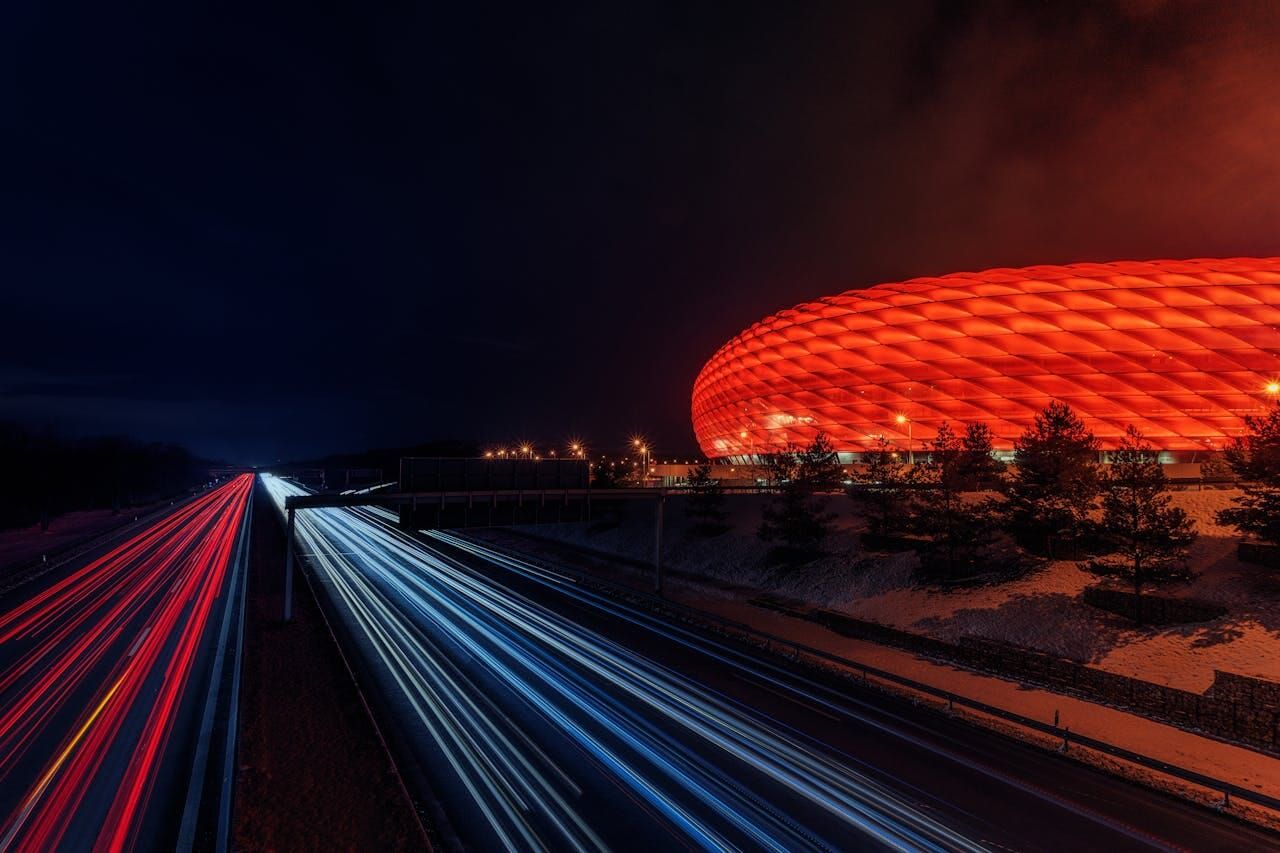 Motorway at night with light trails, a red-lit stadium behind it